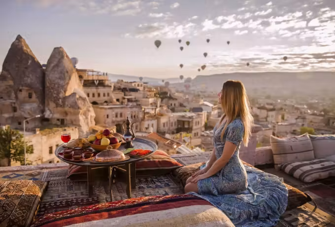 Woman at a dressed board on a woven terrace, carved homes and tufa filling the frame, Cappadocia