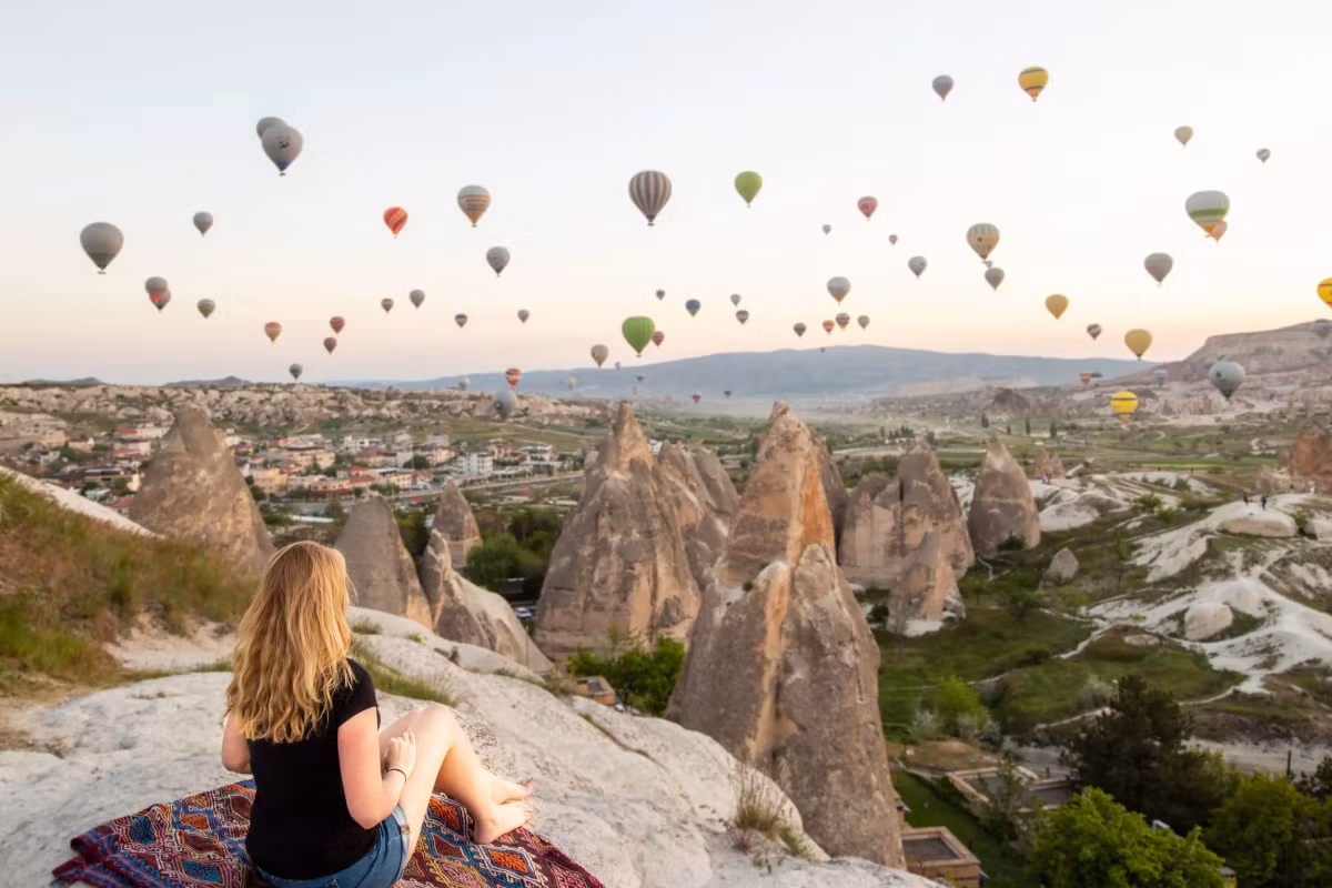 Perched on a printed mat at the lip of a shelf, fabric moving above bleached tufa, Cappadocia