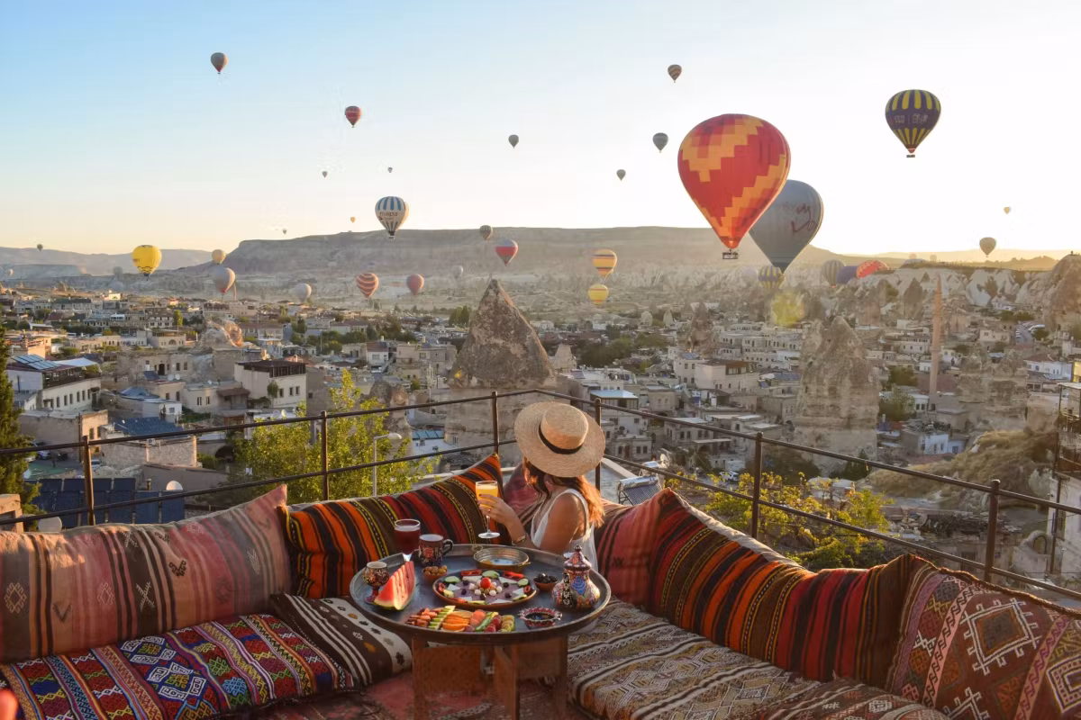 Wide brim on a woven terrace as a big crimson and white envelope passes low over the town, Cappadocia