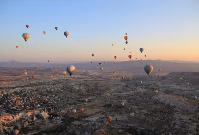 Envelopes stacked at every level across a wide daybreak sky, town and worn valleys far below, Cappadocia