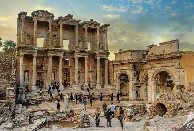 Amber and violet cloud massing over the Celsus front and its arched neighbour as people cross, Ephesus