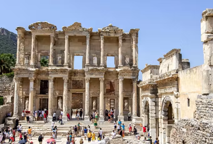 Steps below the Celsus front full of people under a hard noon sky at Ephesus