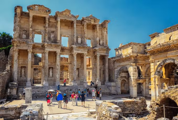 People collected at the foot of the Celsus front, the Roman arch beside it under clear turquoise, Ephesus
