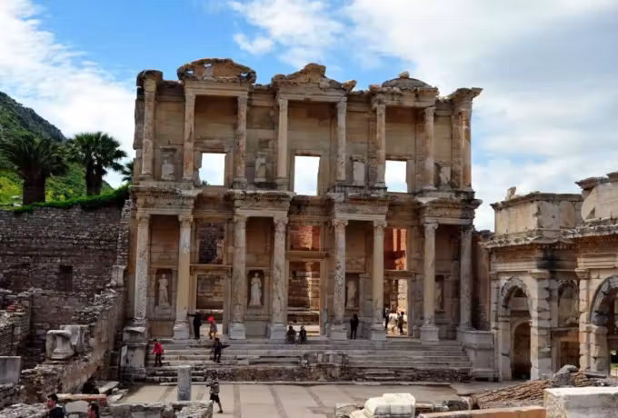 Bright overcast over the Celsus front with a lush slope behind and people on the court, Ephesus