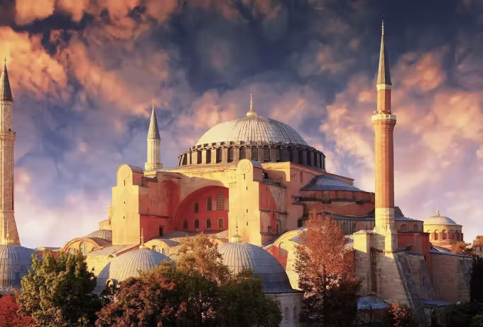 Dramatic autumn weather over a building lit gold above trees in seasonal colour, Istanbul