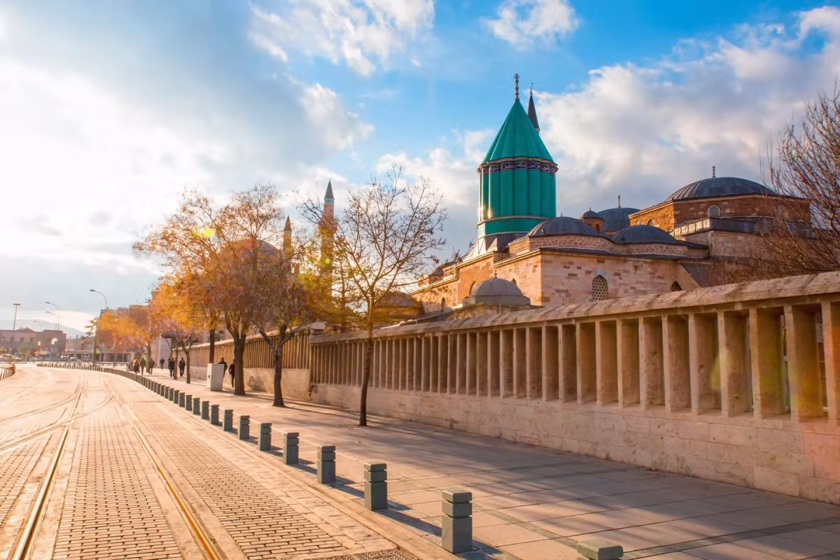 Arcaded screen wall down a broad paved avenue in Konya, the teal cone showing above the roofs