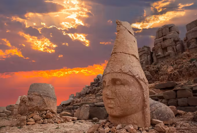 Head in a pointed cap at Nemrut with cloud burning fire-red behind the platform