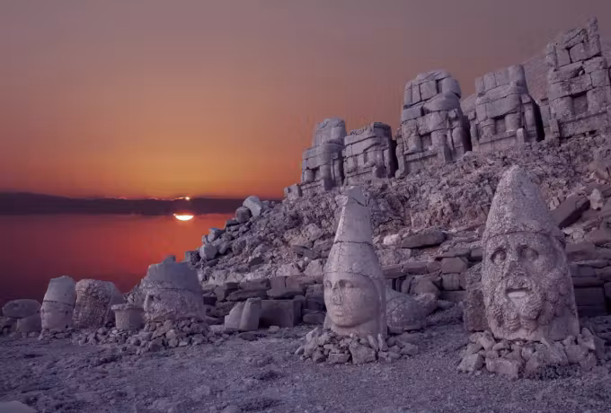 Sun sitting right on the skyline behind the heads and seated rank at Nemrut