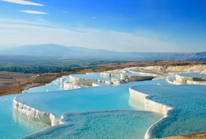 Cultivated flats and one white peak lie beyond rimmed hollows brimming with colour, Pamukkale