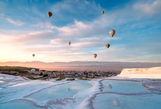 Envelopes climbing a pale early sky over the chalk shelves, colour repeated in the water, Pamukkale