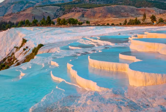 Mineral rims cupping colour beneath a timbered bank just turning for the season, Pamukkale