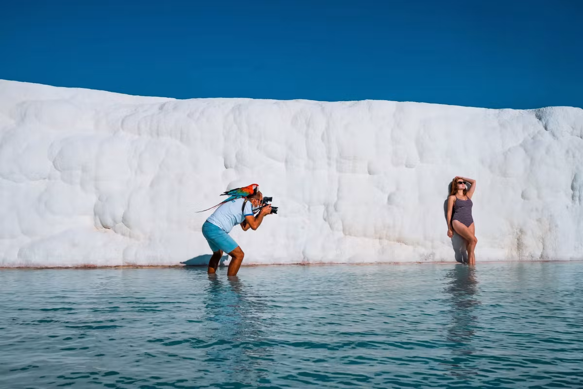 Photographer standing in the shallows to shoot a model against the towering chalk face, Pamukkale