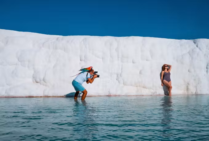 Photographer standing in the shallows to shoot a model against the towering chalk face, Pamukkale