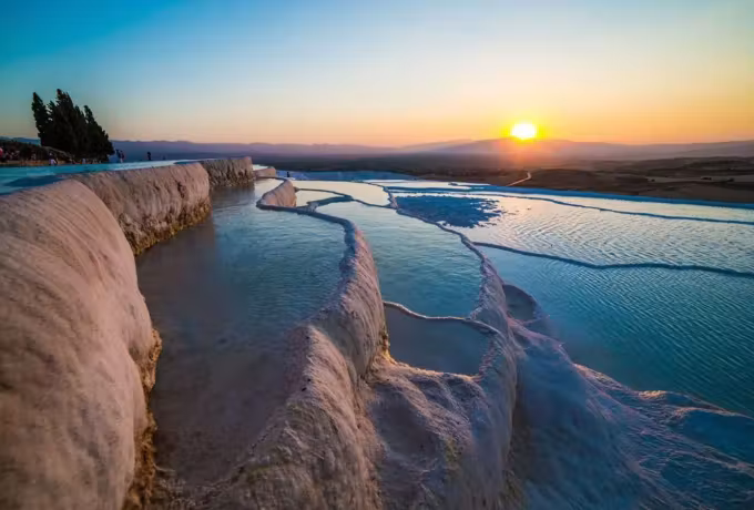 Water running in a long lane between chalk lips with the sun low over far mountains, Pamukkale