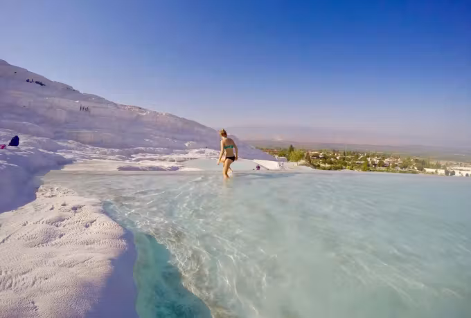 Figure on the rim of a broad shallow sheet with mineral flank and cropland past it, Pamukkale