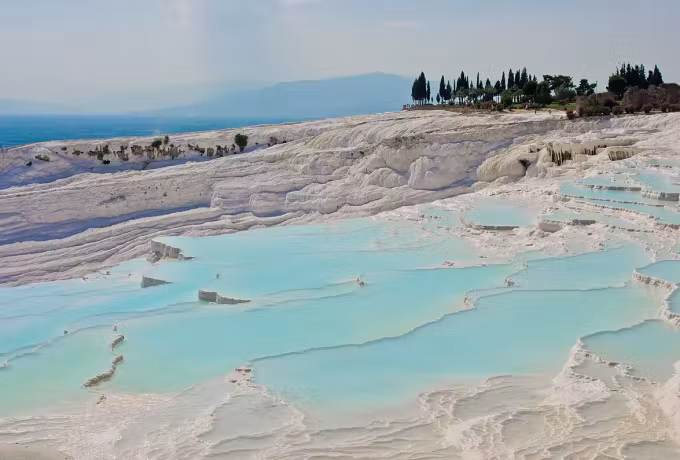 Broad flat water lying in the chalk below a line of trees along the upper crest, Pamukkale