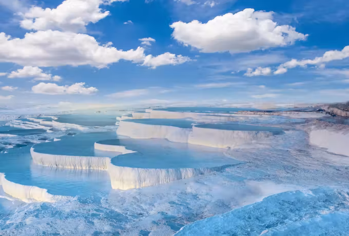 Extended mineral rim spilling into one broad washed-out sheet under rounded cloud, Pamukkale