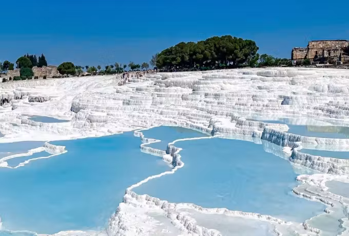 Tiered blue water in the chalk below the trees and old walls on the plateau above