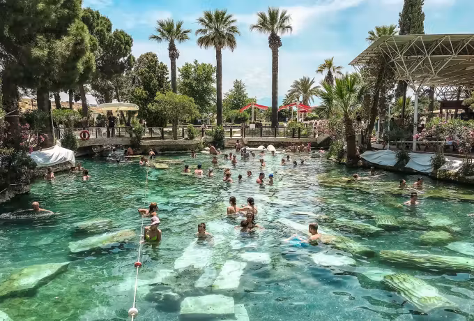 Busy warm water in the Antik Havuz with cut marble on the bottom under palms and pines