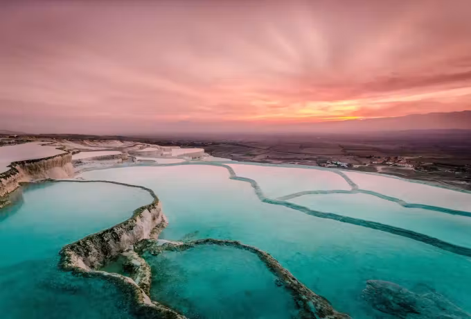 Snaking green-blue water glowing in the chalk under a wide rose and gold evening