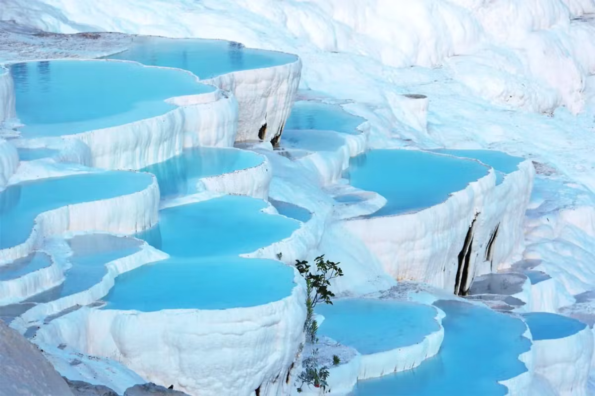 Stacked layers of white lips holding bright mineral water across the Pamukkale flank
