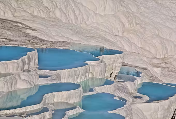 Little blue pools at the base of a polished chalk flank on the Pamukkale hillside