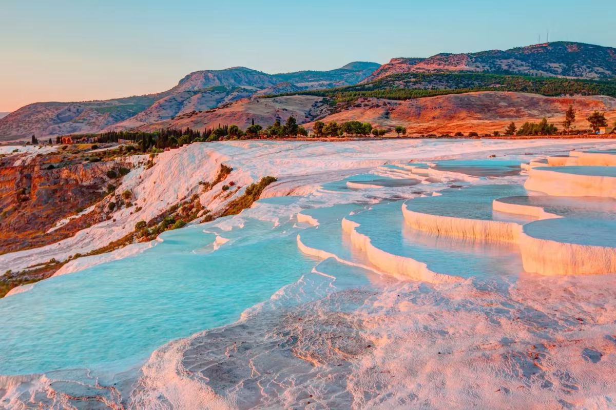 Shell-edged white pools holding pale water as the hills behind warm with the last sun, Pamukkale