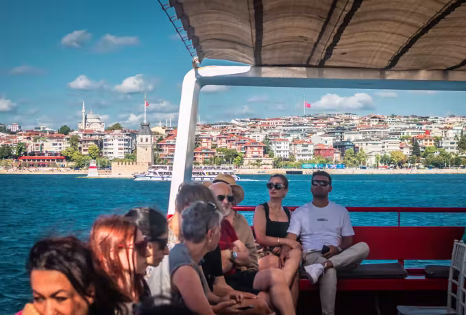 Red benches beneath the awning of an Istanbul boat as the shoreline slides by