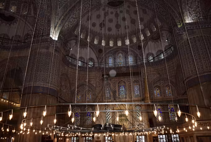Low hanging lamps lighting the prayer floor under painted cupolas and pointed arches, Istanbul