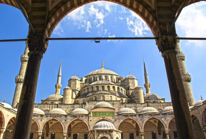 Forecourt arch framing cupolas and towers against a sky scattered with cloud, Istanbul