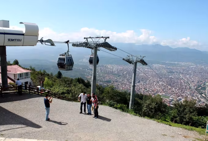 Cabins swinging out over the ridge from an open Uludag station, Bursa far down on the plain
