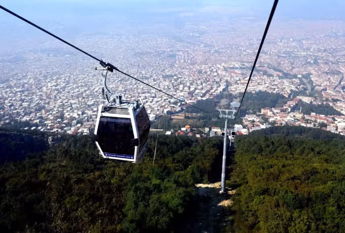 Teleferik cabin on its way down over timbered slopes, Bursa rooftops hazy to the horizon