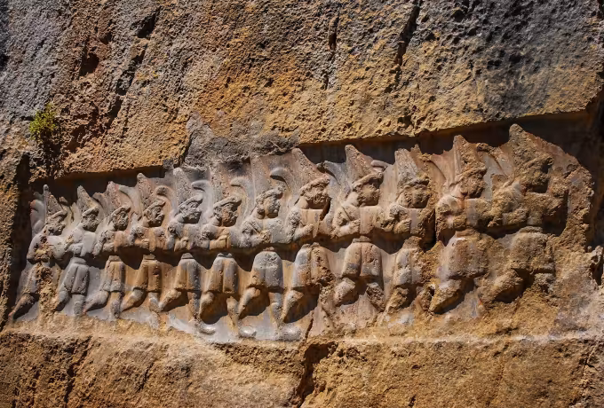Tight rank of miniature walkers worked into a weathered rust-coloured face at Hattusa