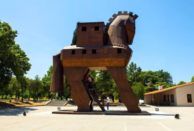 Angular dark timber figure of a horse on the paving beside the Troy site buildings