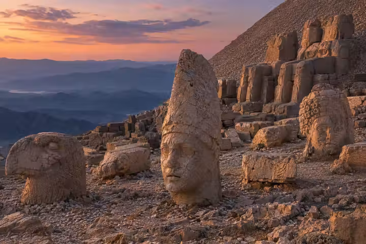 Weathered stone heads and summit monuments at Mount Nemrut in warm sunset light, with layered mountains beyond