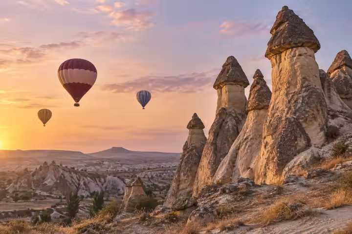 Three hot air balloons beside tall capped fairy chimneys in Cappadocia in warm sunrise light