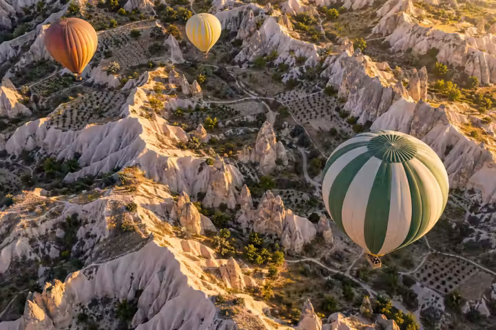 Aerial view of three hot air balloons above Cappadocia rock ridges and orchards in sunrise light