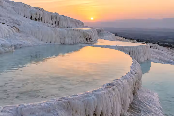 Golden light reflected in shallow Pamukkale pools bordered by curved white travertine terraces