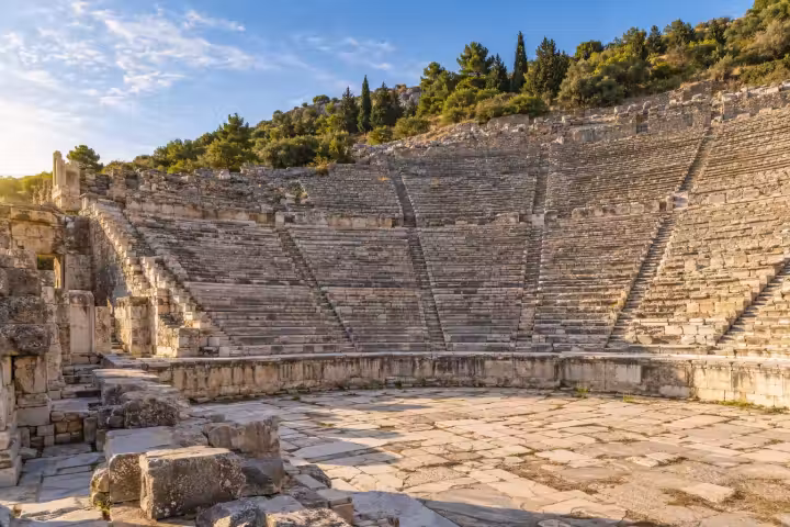 Curved ancient theatre seating and stone ruins at Ephesus in warm morning light