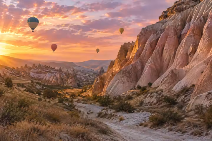 Four hot air balloons above a Cappadocia valley beside pink rock walls at sunrise