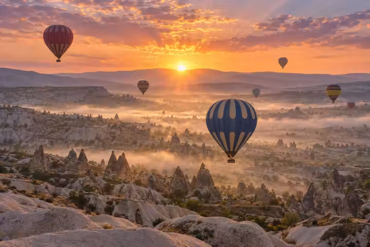 Blue and ivory hot air balloon above misty Cappadocia fairy chimneys at golden sunrise