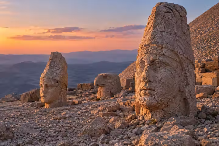 Weathered stone heads and an eagle sculpture on Mount Nemrut in warm sunset light