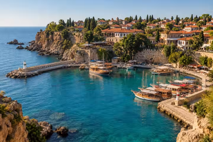 Wooden boats on turquoise water beneath the red-roofed old town in Antalya