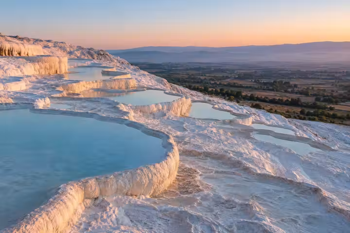 Shallow blue pools on Pamukkale white terraces above the valley in warm dawn light