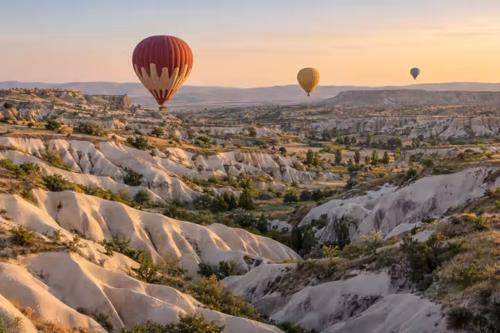Three hot air balloons above white Cappadocia valleys in warm sunrise light