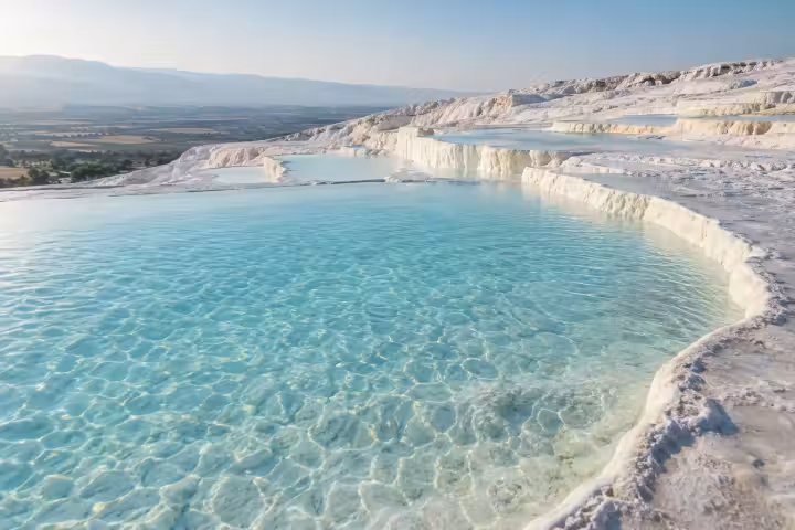 Clear turquoise water and white travertine terraces at Pamukkale in morning light