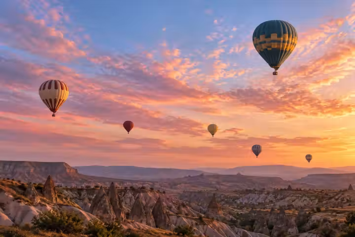 Hot air balloons over Cappadocia beneath peach and rose sunrise clouds