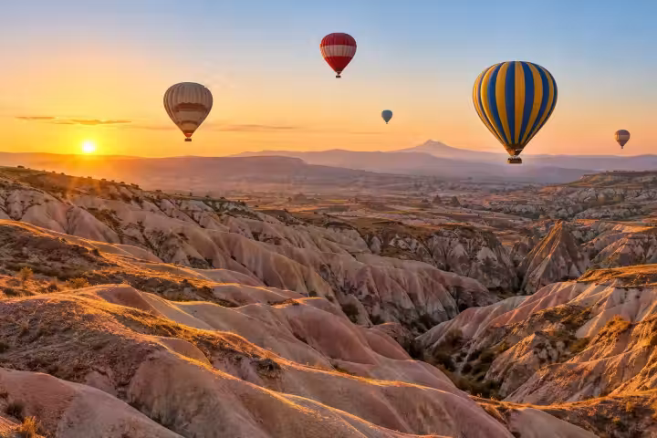 Blue and gold hot air balloon over Cappadocia rose-coloured ridges at sunrise