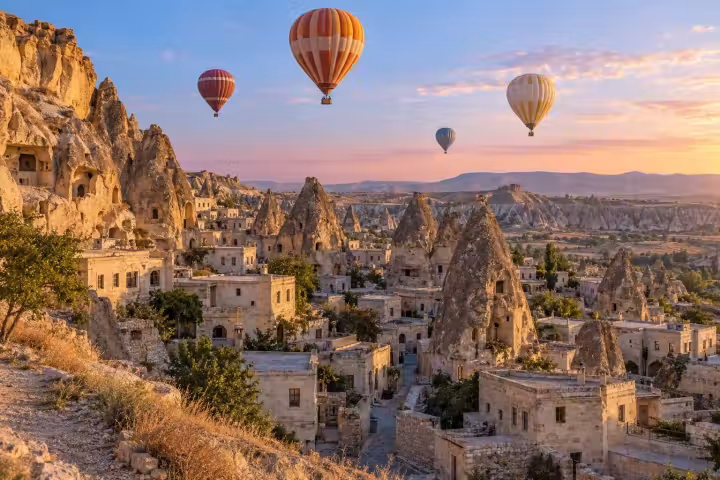 Orange and ivory hot air balloon above Cappadocia stone houses and cave dwellings at sunrise