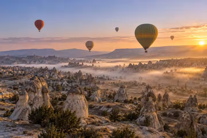 Hot air balloons above misty Cappadocia fairy chimneys in golden sunrise light